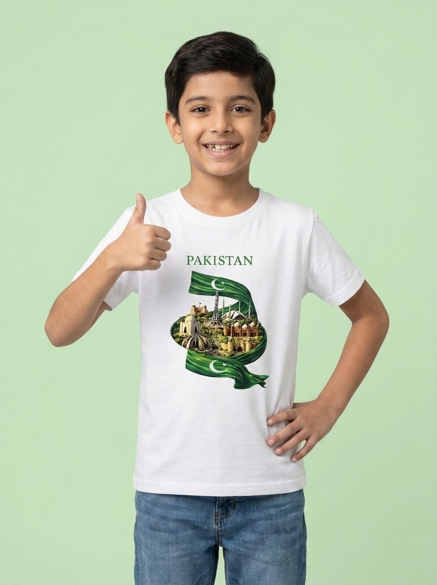 A young boy wearing a white t-shirt with a green and gold graphic of the Pakistan flag and cityscape, paired with blue jeans, standing against a solid light green background.