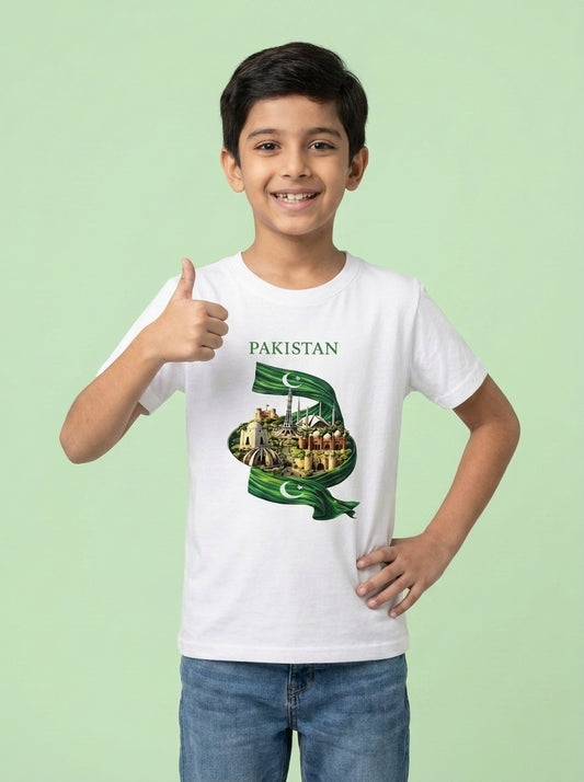 A young boy wearing a white t-shirt with a green and gold graphic of the Pakistan flag and cityscape, paired with blue jeans, standing against a solid light green background.
